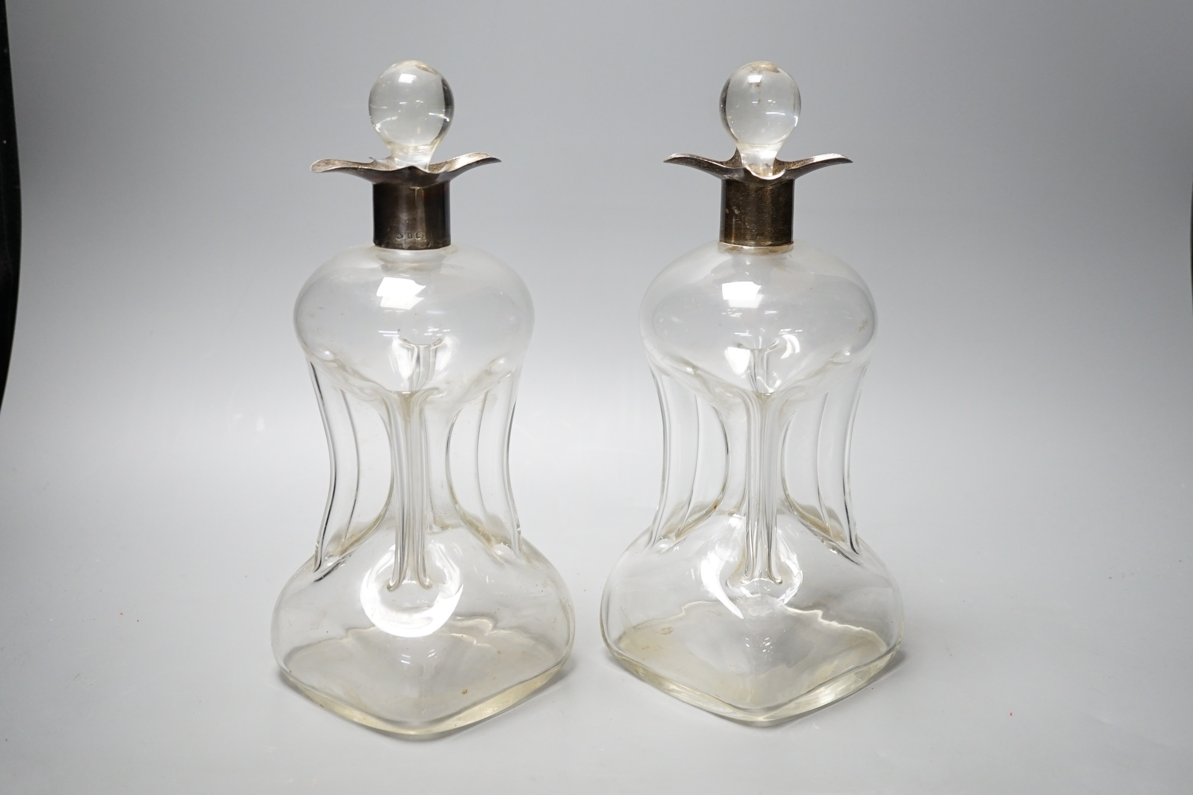 A pair of Edwardian silver mounted hourglass shaped glass decanters with stoppers, by William Hutton & Sons, Birmingham, 1903, overall height 27.5cm.